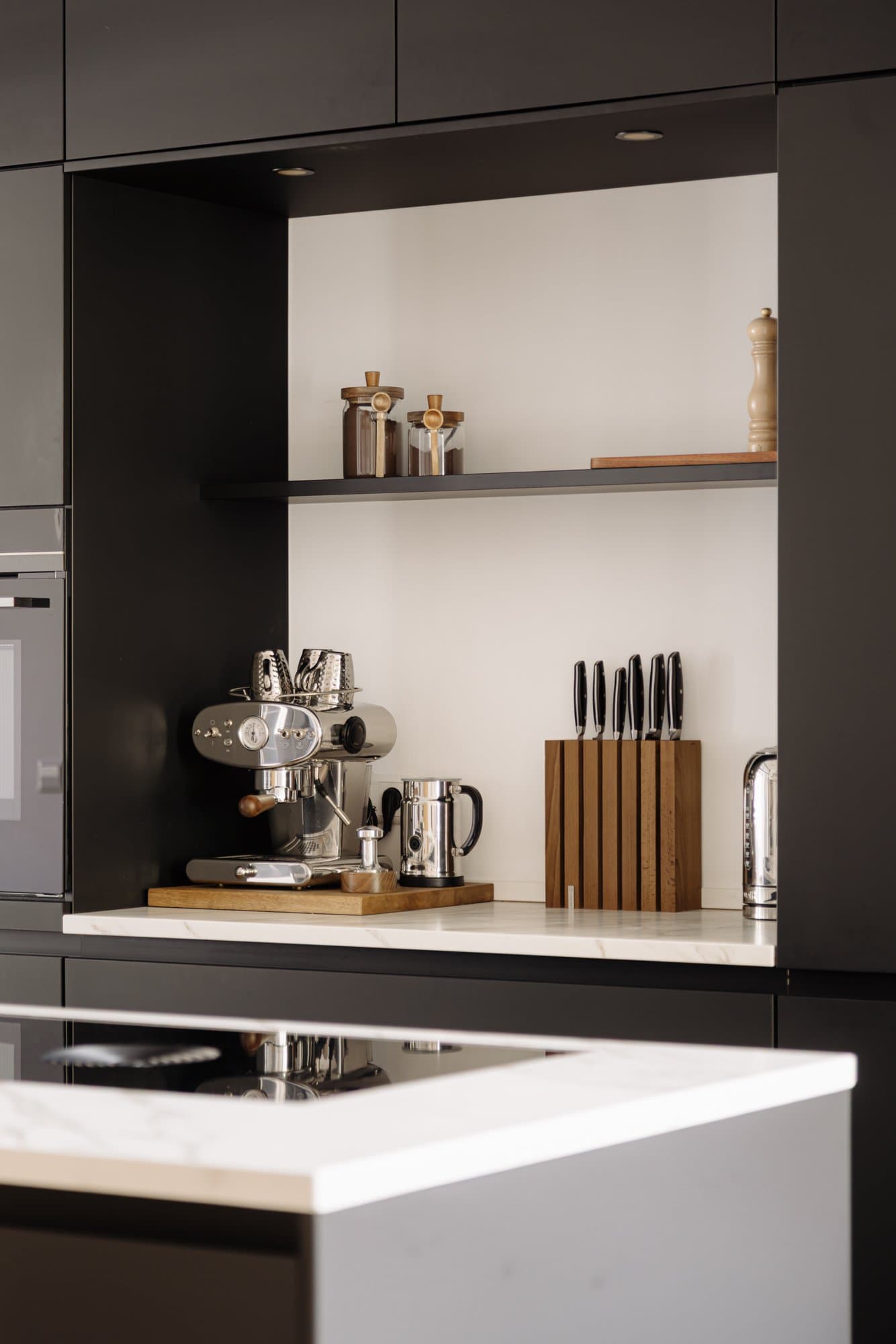 Detail van het werkblad met espressomachine en messenblok tegen de zwarte wand