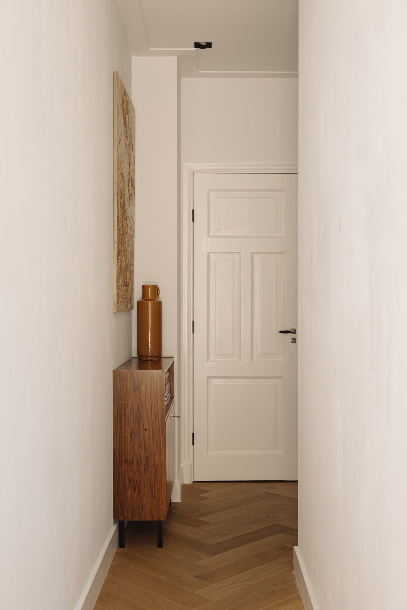 Een opgeknapte witte paneeldeur naast een houten kastje