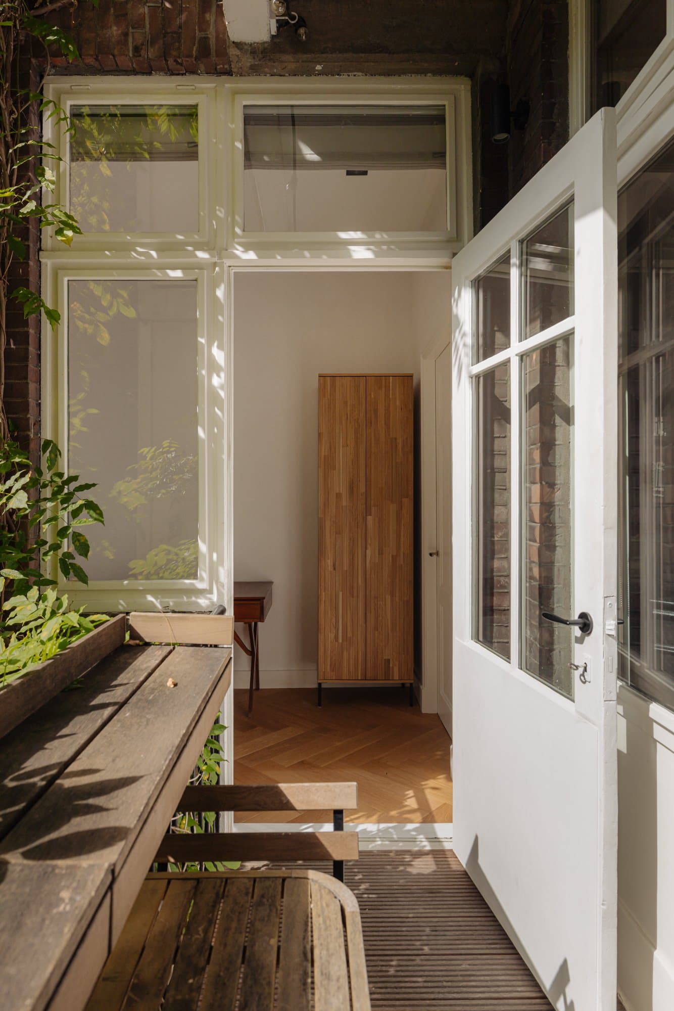 De serre met planten en houten kast, met daglicht door de openslaande deuren