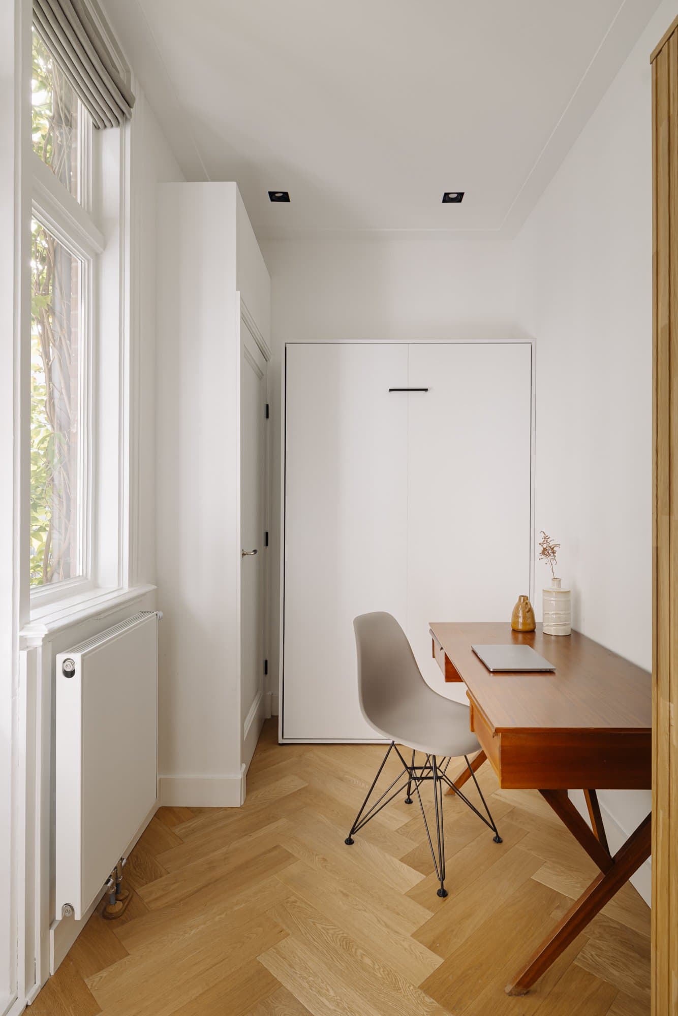 De werkplek bij het raam met bureau en stoel tegen de witte wand