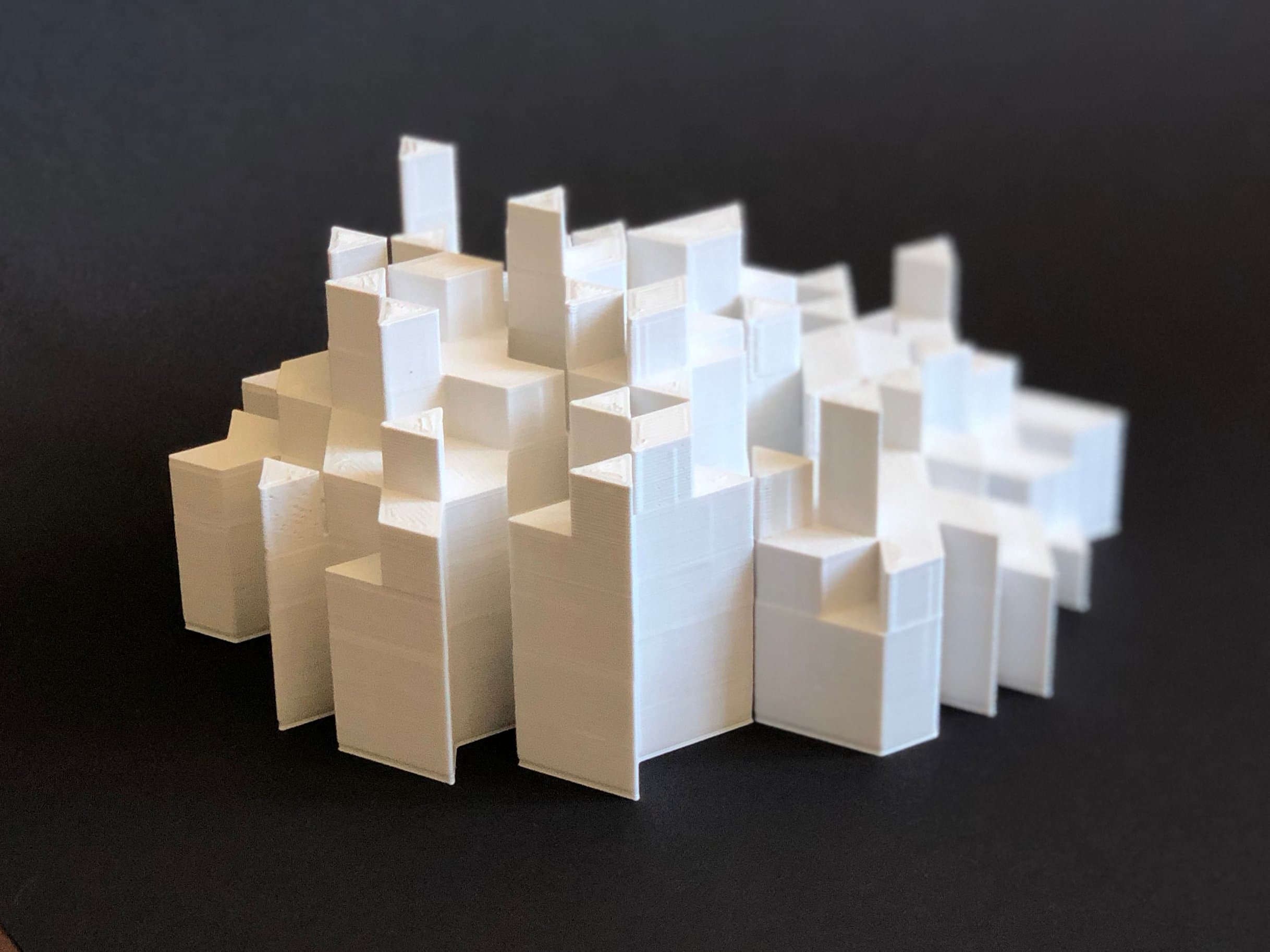 Het 3D-geprinte model van dichtbij: witte gestapelde volumes tegen een zwarte achtergrond