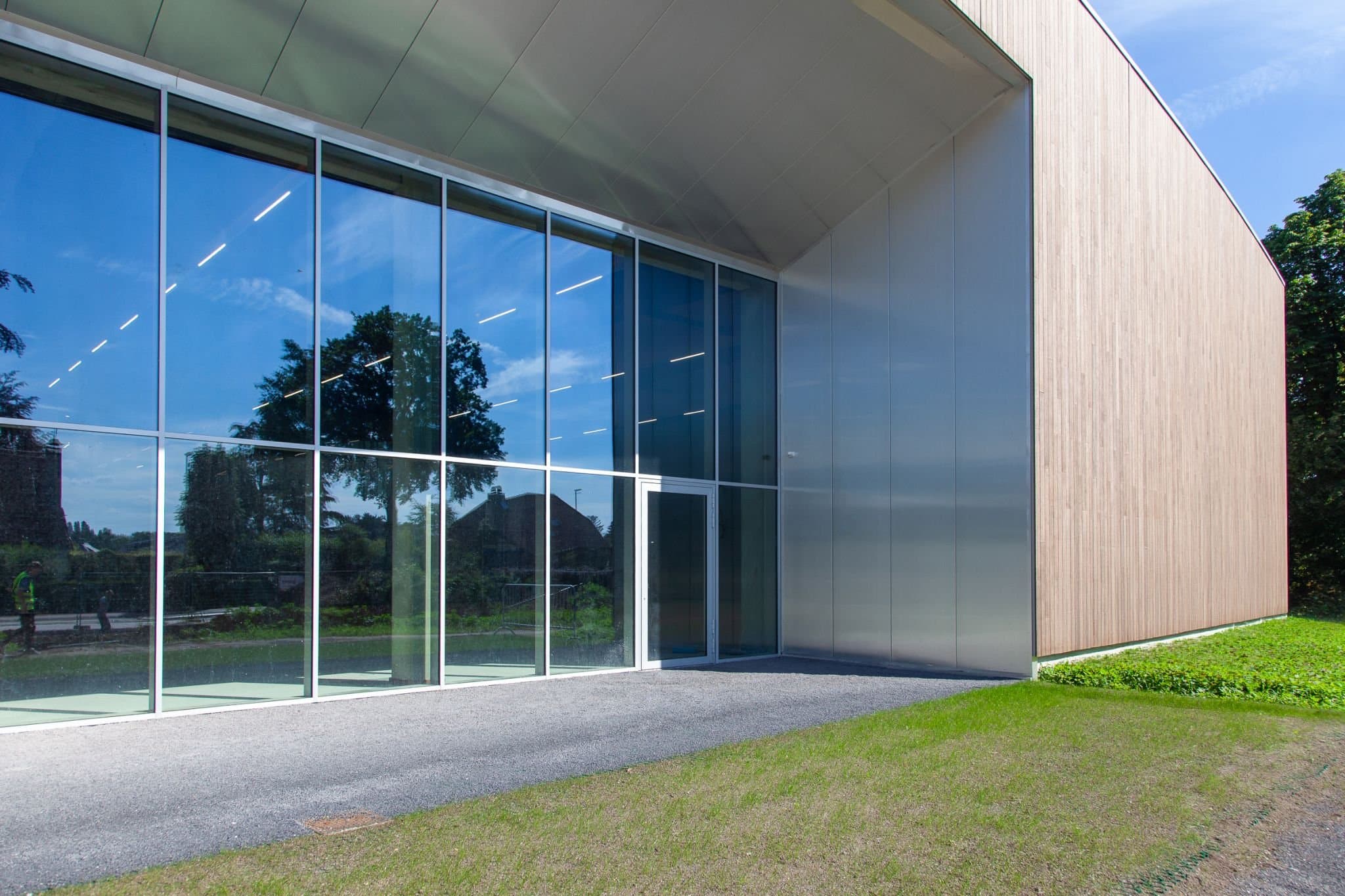 Detail van de vliesgevel waarin het park weerspiegelt, naast het houten volume van de sporthal
