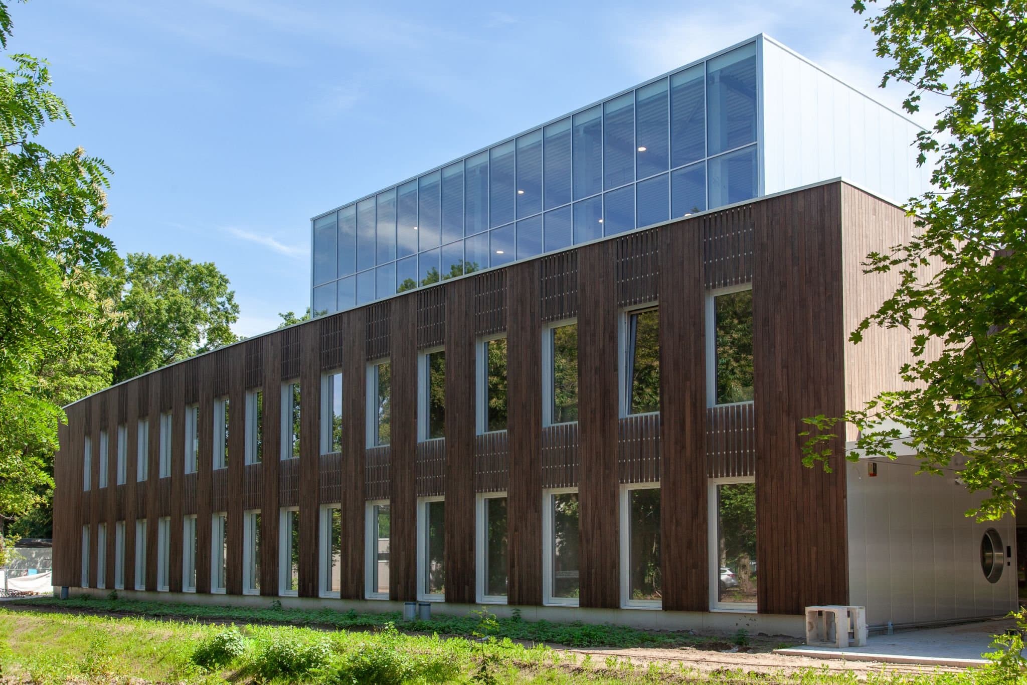 Hoekaanzicht van het gebouw: houten gevel met verspringende raamopeningen, met de glazen opbouw erboven