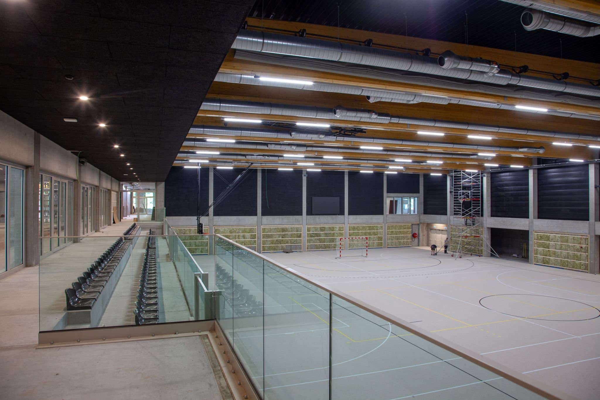 De sporthal gezien vanaf de galerij, met uitschuifbare tribune en het houten dak boven het speelveld