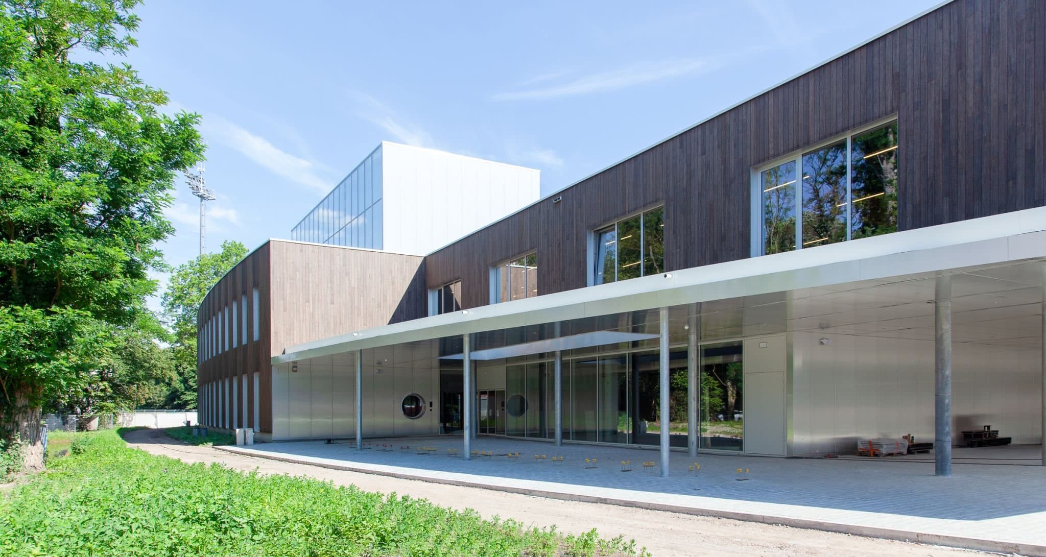 Het opgeleverde sportcomplex met houten gevel en doorlopende luifel boven de glazen plint